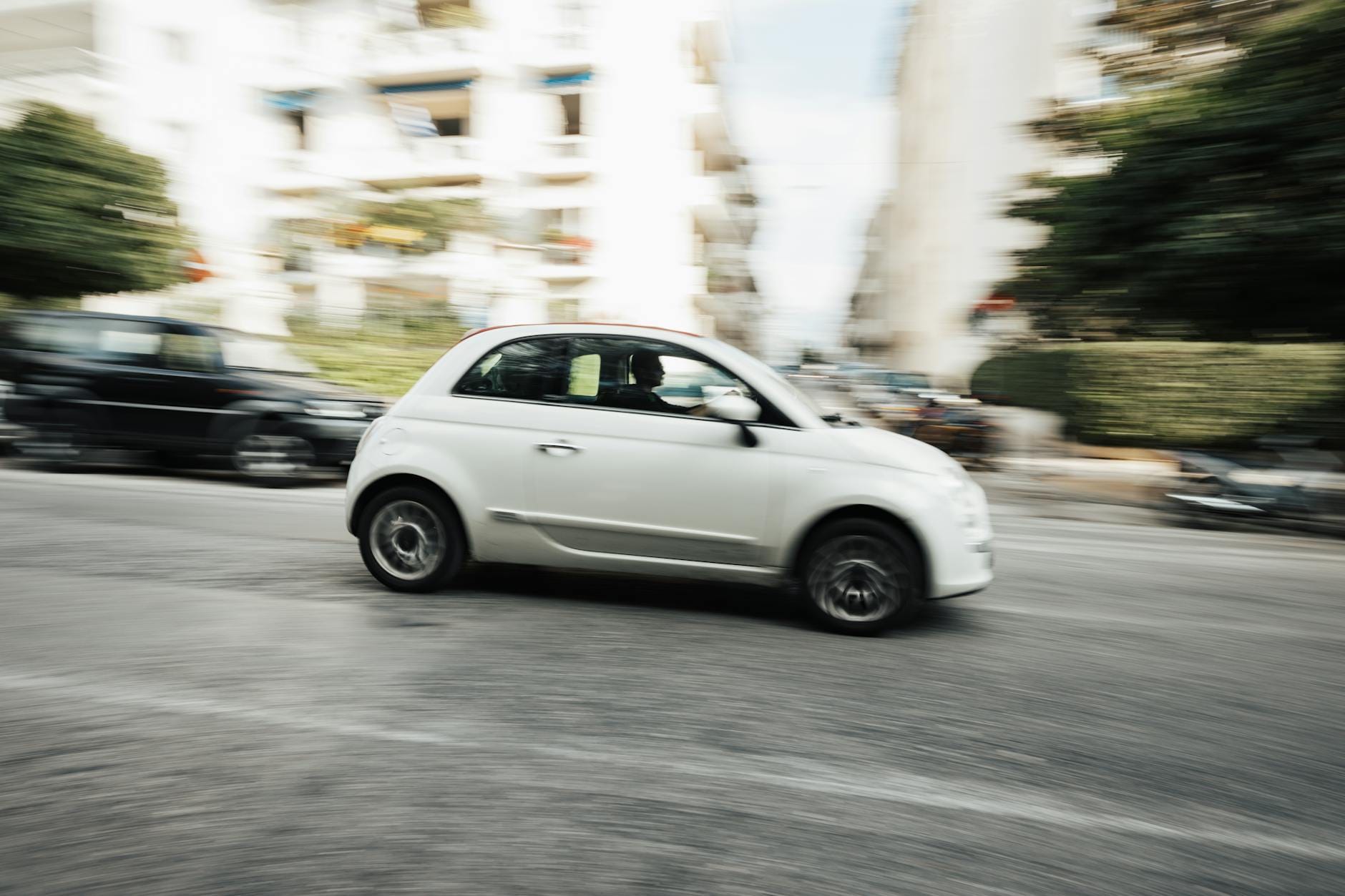 Biały kompaktowy samochód jedzie szybko ulicą miasta