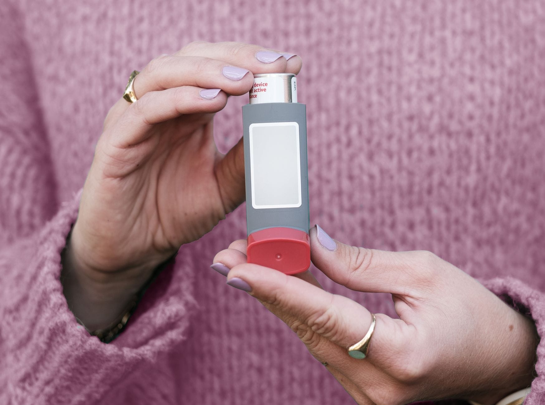 Dłonie kobiety trzymające inhalator na tle różowego swetra