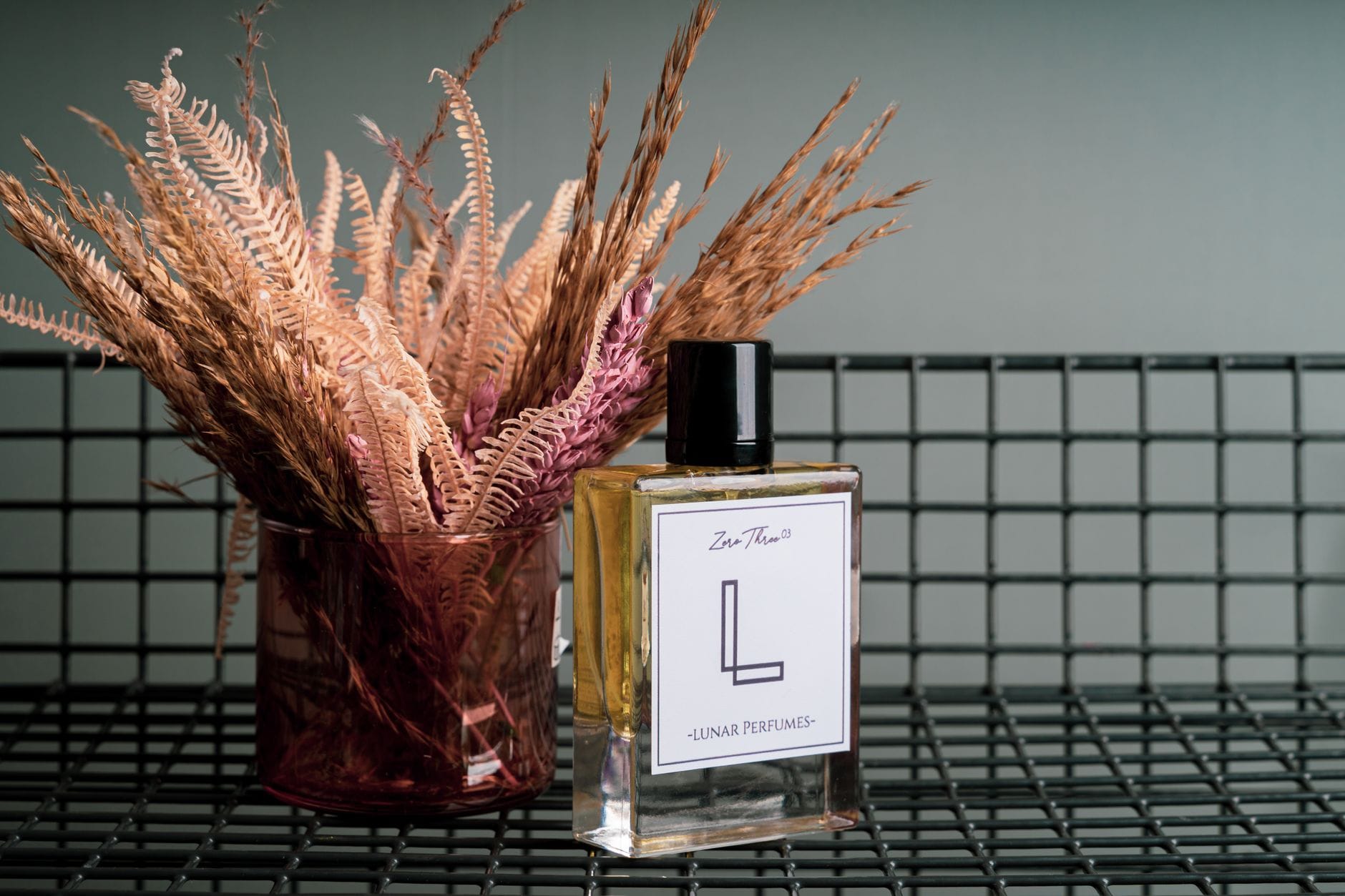 Elegancki flakon perfum z wysuszonymi kwiatami na metalowej siatce